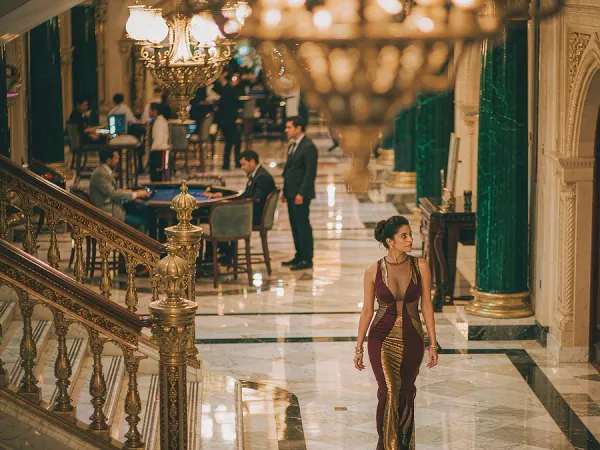 six6s + Woman in a maroon and gold dress walking through a chandelier-lit casino lobby